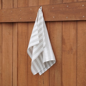 Puede incluir: Un paño de cocina a rayas blancas y grises colgado de un gancho sobre un fondo de madera.