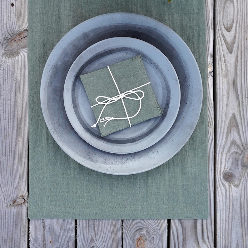Sage green linen table runner on a wooden dining table with ceramic plates and natural table setting