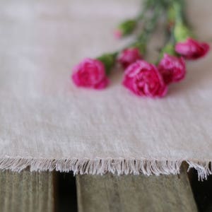 May include: A white linen table runner with a fringed edge and pink carnations.