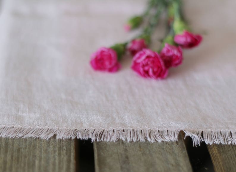 May include: A white linen table runner with a fringed edge and pink carnations.