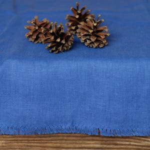 May include: A blue linen table runner with a fringed edge. Three pine cones are arranged on the runner.