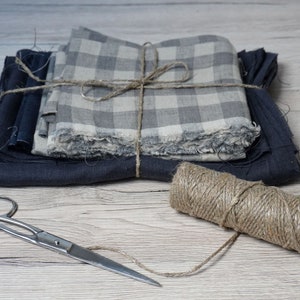 Könnte beinhalten: Ein Stapel Stoff in Grautönen und Blau ist mit Schnur zusammengebunden. Eine Schnurspule und eine silberne Schere liegen auf einer Holzoberfläche.