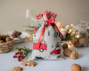 Puede incluir: Una bolsa de regalo de Navidad roja y blanca con una cinta roja y un patrón de coches rojos y árboles de Navidad. La bolsa está sobre una mesa blanca con otras decoraciones navideñas.