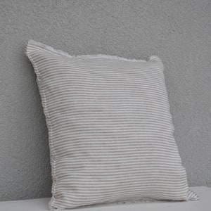 May include: A white and beige striped pillow with a frayed edge. The pillow is made of a soft, linen-like fabric.