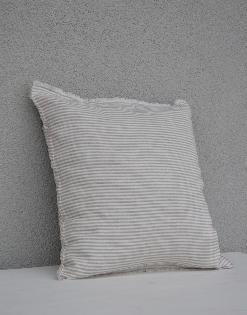 May include: A white and beige striped pillow with a frayed edge. The pillow is made of a soft, linen-like fabric.