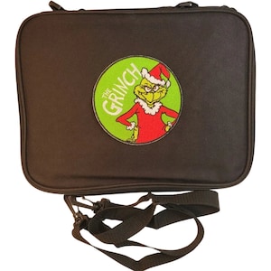 May include: Black rectangular carrying case featuring a circular patch with the Grinch character in a Santa hat and red suit. The patch is surrounded by a green circle with the words "THE GRINCH". Includes a black shoulder strap.
