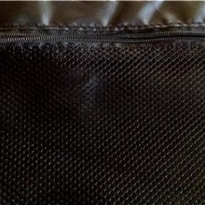 May include: Close-up of a black mesh fabric with a zipper at the top. The zipper is dark gray and has a small metal pull. The mesh has a diamond pattern and is likely part of a bag or other container.