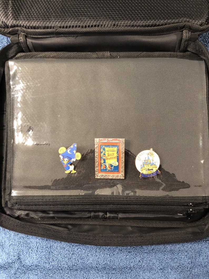 May include: Black zippered pin carrying case with clear plastic sleeves. Three Disney pins are visible: Donald Duck in a wizard hat, a "Silly Symphonies" pin, and a pin with Cinderella's castle.