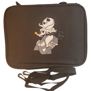 Puede incluir: Bolso rectangular negro con cierre de cremallera y correa de hombro desmontable. El bolso presenta una imagen bordada de Jack Skellington y Zero de Pesadilla antes de Navidad. Los personajes son en negro, blanco y gris.