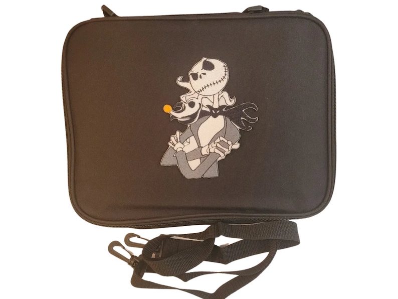 Puede incluir: Bolso rectangular negro con cierre de cremallera y correa de hombro desmontable. El bolso presenta una imagen bordada de Jack Skellington y Zero de Pesadilla antes de Navidad. Los personajes son en negro, blanco y gris.