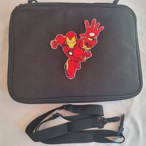 May include: Black rectangular bag with a red and yellow Iron Man patch. The bag has a zipper closure and a detachable black shoulder strap. The Iron Man patch depicts the superhero in a dynamic pose.