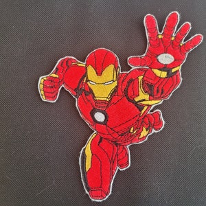 May include: Embroidered patch featuring Iron Man in a dynamic pose, with his right hand extended. The patch showcases a red and yellow color scheme, with detailed stitching outlining the superhero's iconic suit. The patch is likely for clothing or accessories.