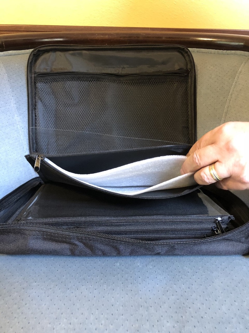 May include: Black zippered organizer case with multiple compartments. The case is open, revealing a mesh pocket, clear plastic sleeves, and a padded interior. A hand with a ring is visible.