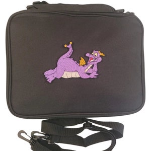 May include: Black rectangular bag with a zipper closure and a detachable shoulder strap. The bag features an embroidered purple dragon with yellow accents. The dragon is lying down with its head resting on its hand.