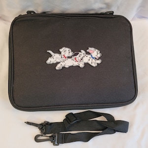 May include: Black rectangular carrying case with a zipper closure and a detachable shoulder strap. The case features an embroidered patch of three Dalmatian puppies with black spots and red collars.