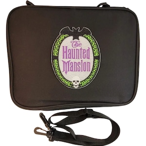 May include: Black rectangular bag with a zipper closure and a detachable shoulder strap. The bag features an embroidered emblem with the words "The Haunted Mansion" in purple, a skull, and a bat.