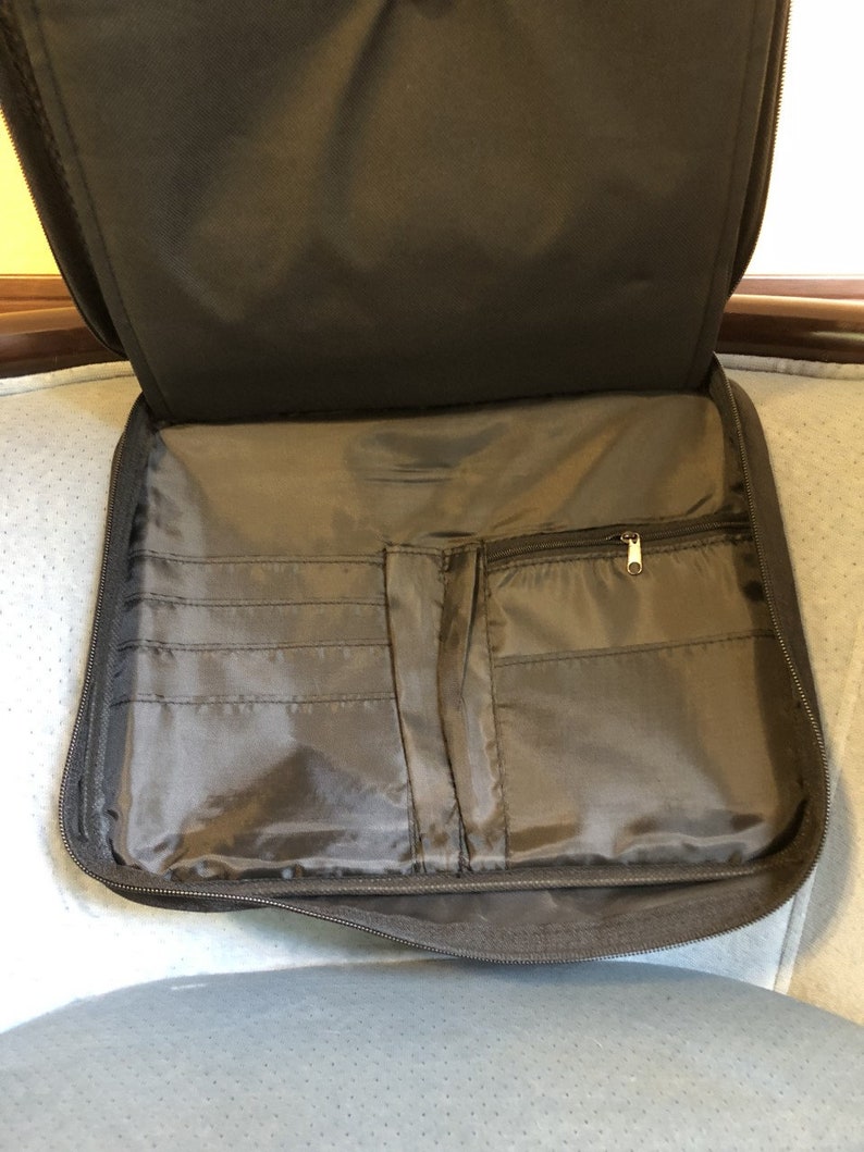 May include: Open, dark gray zippered portfolio with multiple interior pockets and a zippered compartment. The portfolio is made of a smooth, durable material and is designed to hold documents and other items. The interior features several card slots.