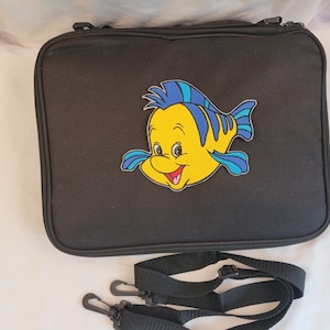 May include: Black rectangular case with a zipper closure and a Flounder patch. The patch features a yellow fish with blue accents. Includes a black shoulder strap with two clips.