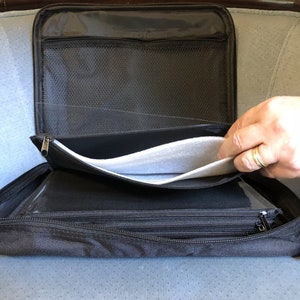 May include: Black zippered organizer case with multiple compartments. The case is open, revealing a mesh pocket, clear plastic sleeves, and a padded section. The interior is black and the exterior is a durable, textured fabric.