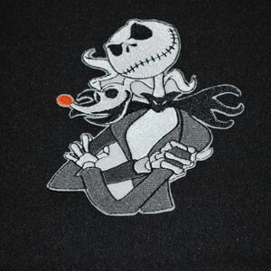 Puede incluir: Parche bordado con Jack Skellington y Zero de Pesadilla antes de Navidad. Jack, con una cara cosida, lleva un traje negro, Zero tiene una nariz roja. El parche es en tonos negros, blancos y grises.