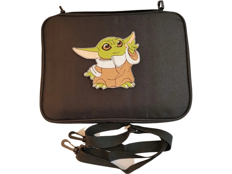 Puede incluir: Bolso rectangular negro con una imagen bordada de un personaje alien&iacute;gena verde con ojos grandes y orejas puntiagudas. El bolso tiene una correa negra para el hombro con dos clips negros.