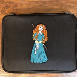 Puede incluir: Estuche negro rectangular con cremallera con un parche bordado colorido de una mujer de dibujos animados con cabello rizado rojo, que lleva un vestido turquesa y sostiene un arco. El estuche está hecho de tela duradera.