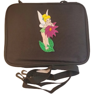Peut inclure: Sac rectangulaire noir avec fermeture éclair, orné d'une image brodée colorée d'une fée tenant une grande fleur rose. Comprend une bandoulière noire réglable avec des fermoirs métalliques.