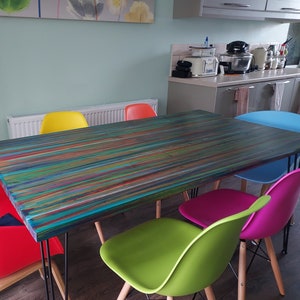 May include: A colorful dining table with a striped wood top and black hairpin legs. The table is surrounded by six brightly colored chairs: red, yellow, green, pink, and blue.