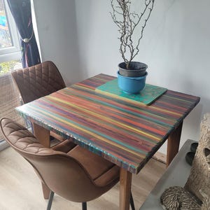 May include: A colorful, multi-striped wooden table with a brown leather chair. The table has a unique, hand-crafted look and is perfect for a small dining area or kitchen.