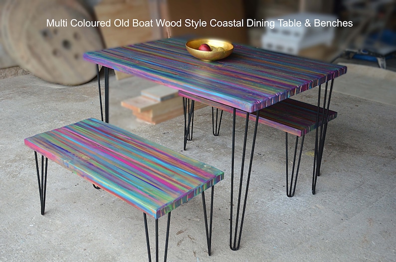 May include: Multi-coloured dining table and two benches made from reclaimed wood with a rainbow finish. The table and benches have black hairpin legs.