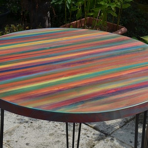 May include: A round wooden table with a colourful striped top. The table has a black metal base with four legs.