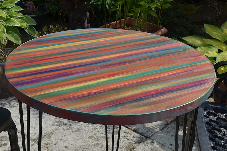 May include: A round wooden table with a colourful striped top. The table has a black metal base with four legs.