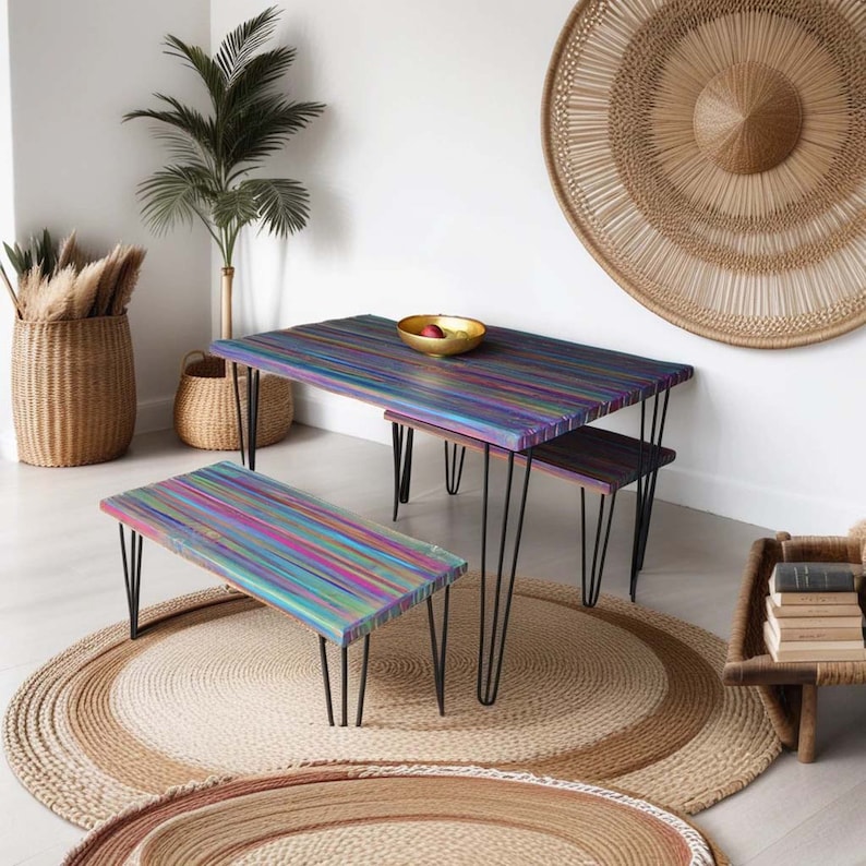 May include: A colourful wooden table and bench set with black hairpin legs. The table and bench have a rainbow stripe pattern. The set is on a jute rug with a round, woven wall hanging in the background.