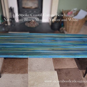 May include: A long, rectangular wooden bench painted in shades of blue, yellow, and white. The bench has black hairpin legs and is sitting on a patterned rug. The text "Bespoke Coastal Cottage Bench" and "Navy, Azure Blues, Mustard Yellow and White" is visible above the bench. The website "www.stevenbowlerdesigns.co.uk" is visible below the bench.
