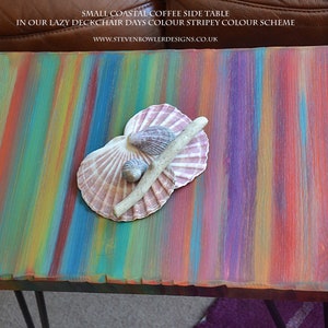 May include: A small wooden side table with a colourful striped paint design. The table has a rustic, coastal feel and is decorated with seashells and driftwood.
