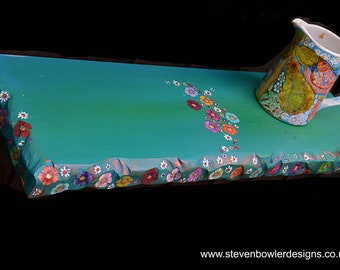 May include: A hand-painted, turquoise-colored wooden tray with a floral design and a matching pitcher. The tray has a rough, textured edge with colorful flowers painted around the border. The pitcher has a floral and fruit design.