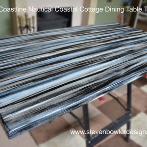 May include: A close-up of a black and white striped wooden table top. The table top has a distressed, weathered look, with white paint streaks and black paint accents. The table top is perfect for a coastal cottage dining room.