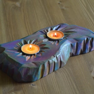 May include: A wooden candle holder with two tealight candles burning. The holder is carved with a sunflower design and has a iridescent finish.