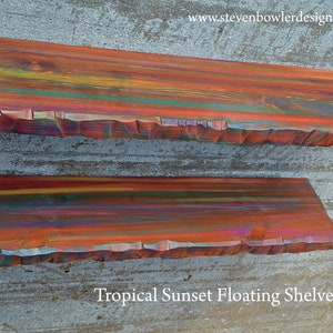 May include: Two floating shelves with a tropical sunset design. The shelves are made of wood and painted with vibrant colors of orange, red, yellow, and blue. The edges have a textured, rough-hewn appearance. The text "Tropical Sunset Floating Shelves" is visible.