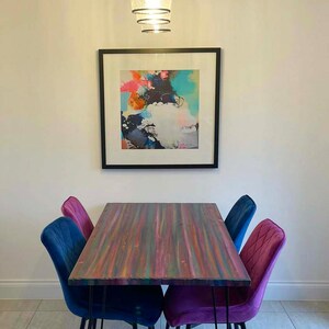 May include: A colourful dining table with a wood top and black hairpin legs. The table is surrounded by four chairs, two blue and two purple.