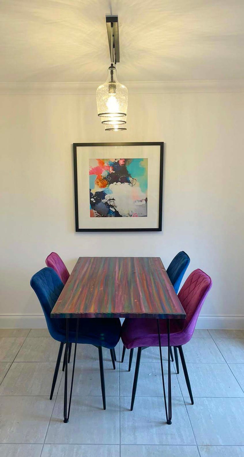 May include: A colourful dining table with a wood top and black hairpin legs. The table is surrounded by four chairs, two blue and two purple.