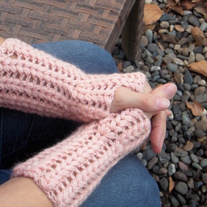 A woman with folded hands wearing pink arm/hand warmers covering her hands and wrists.