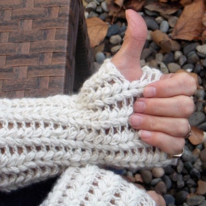 A woman with her left thumb up wearing cream colored arm warmers covering her hands and wrists.