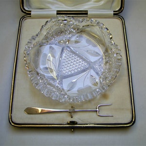 May include: A clear glass serving dish with a decorative cut design, in a white velvet lined box with a silver serving fork and knife.