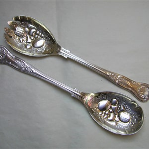 May include: A set of two silver salad servers with ornate handles and a fruit design on the serving ends.