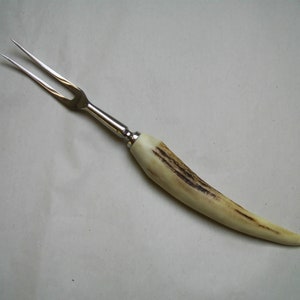 May include: A silver two-pronged fork with a long, curved, light brown antler handle.