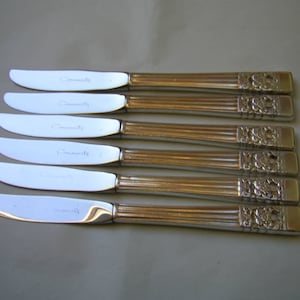 May include: Set of six silver butter knives with ornate handles. Each knife has the word "Community" engraved on the blade.