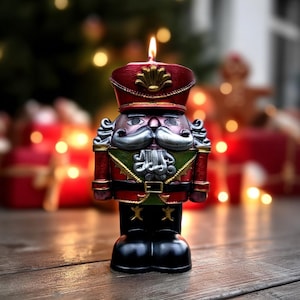 Puede incluir: Una vela decorativa con forma de soldado cascanueces, con una llama encendida. La vela está pintada en rojo, negro, verde y dorado, con un rostro y uniforme detallados. El fondo presenta decoraciones navideñas borrosas.