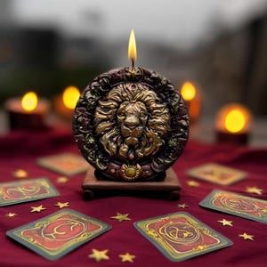 May include: A round candle with a lion's head design, set on a wooden stand. The candle is brown and gold, with a lit wick. Tarot cards and gold stars are scattered on a red surface, creating a mystical theme.