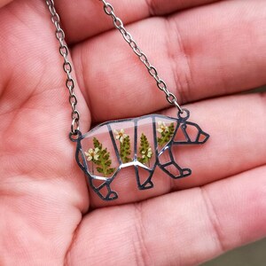May include: A silver chain necklace with a clear resin pendant shaped like a bear. The pendant contains pressed flowers and ferns.